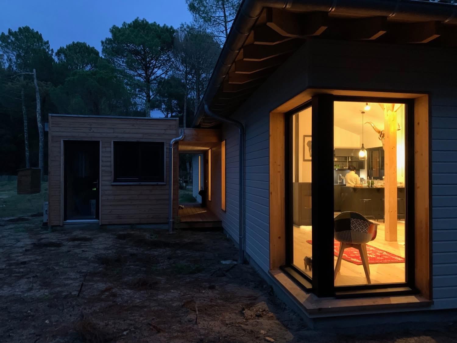 Maison en bois avec grande baie vitrée éclairée au crépuscule